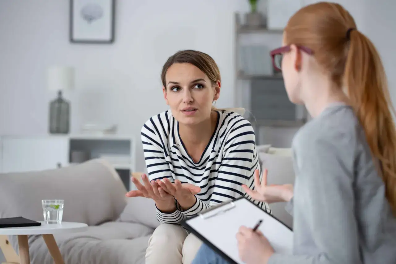 Kobieta w pasiastej bluzce otwarcie mówi o swoich problemach, budując bliską relację terapeutyczną z terapeutką notującą na bieżąco.