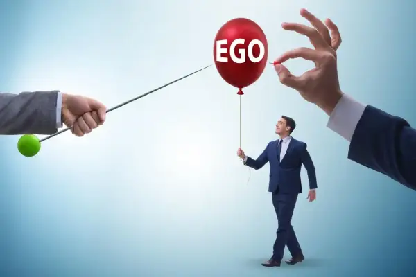 Mężczyzna z balonem "EGO" w ręku, symbolizujący cechy narcyza, zagrożony przez szpilkę.